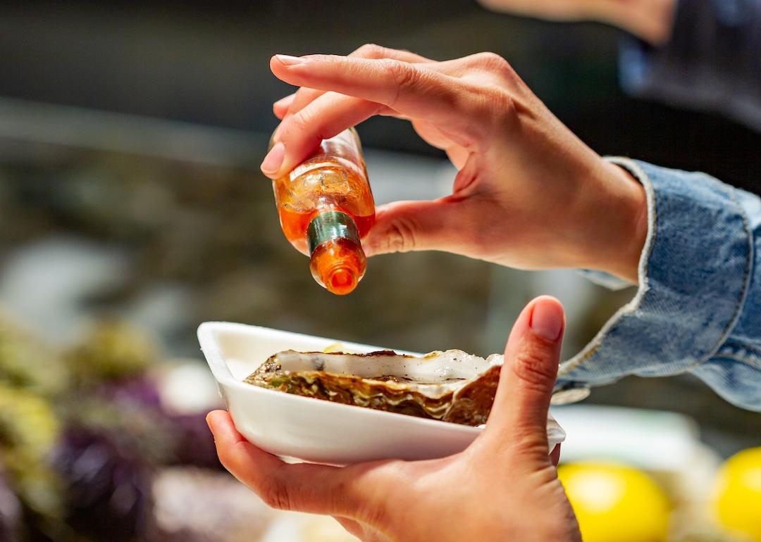 Pouring hot sauce over oyster on white plate.