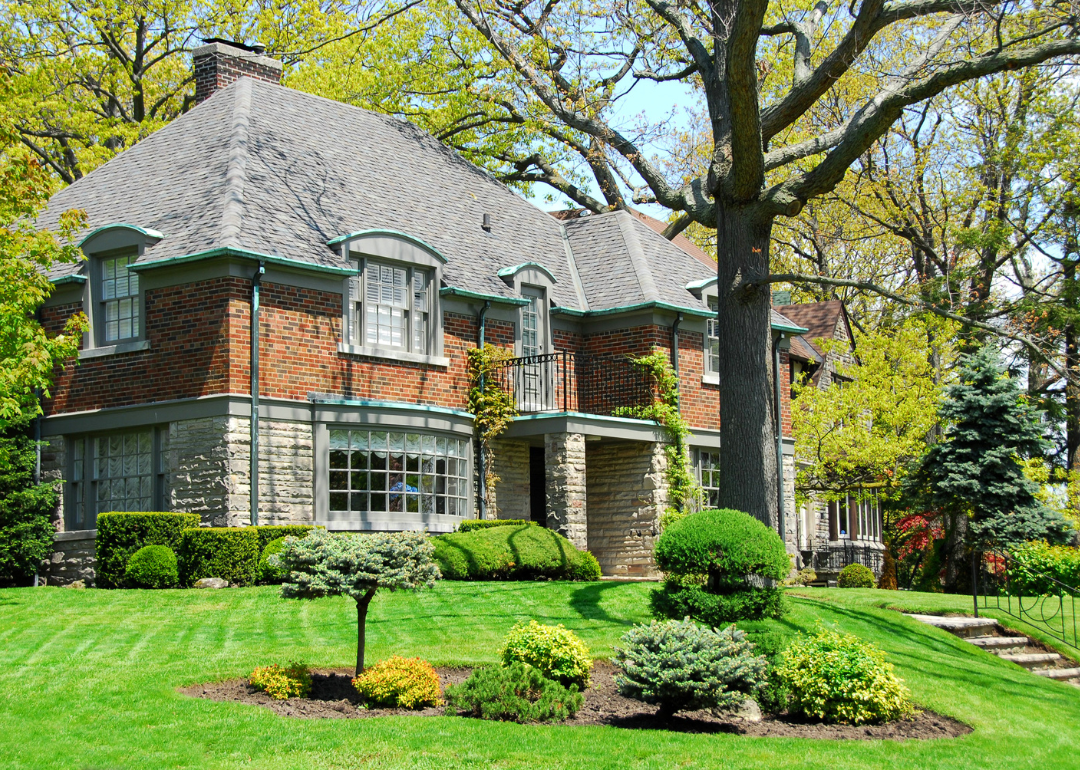 A large two-story brick and stone house with a well-manicured front lawn in an affluent neighborhood.