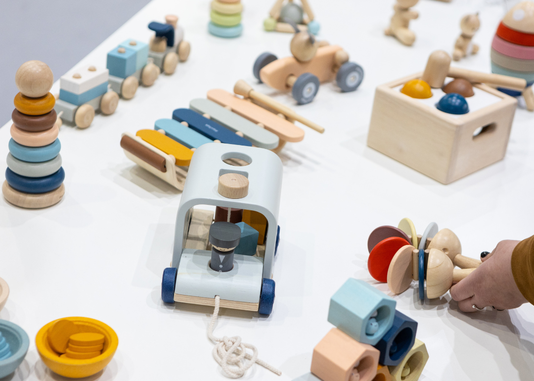 A person's hand placing a wooden toy on a table of wooden toys for baby and infant-aged children.