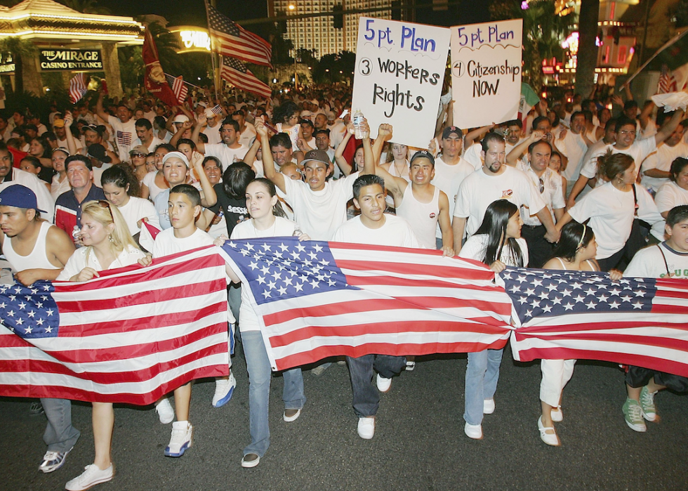 People holding American flags lead a crowd as they walk past The Mirage Casino Entrance.