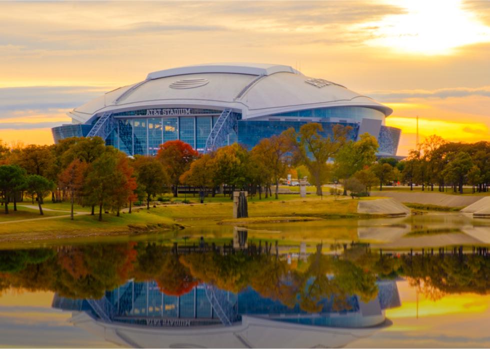 Exterior view of AT&T Stadium with sun setting and reflection in pond.