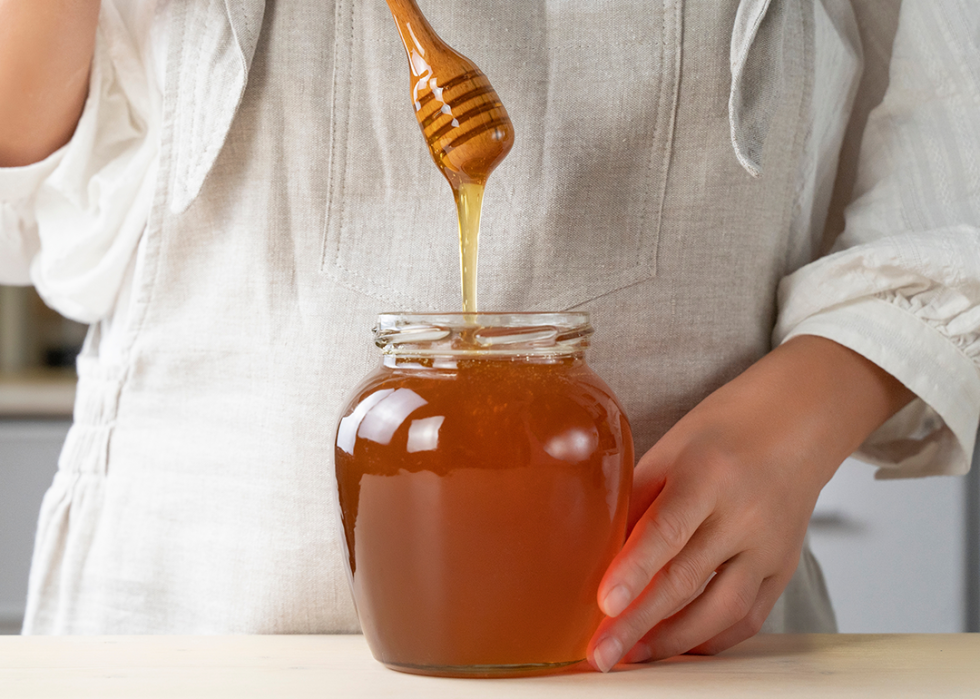 Cropped shot of person holding honey dipper and glass jar.