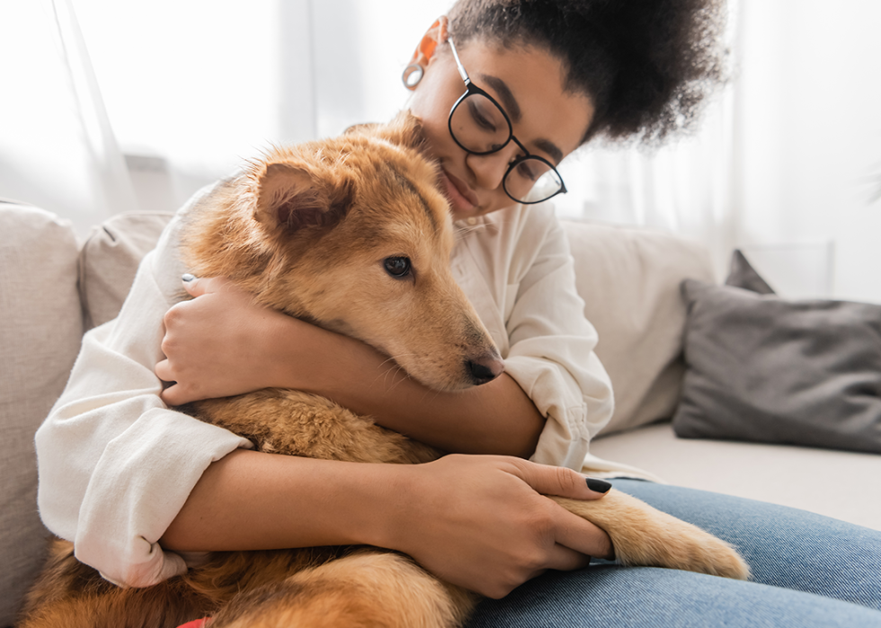 A young woman hugs a large blonde dog on couch.