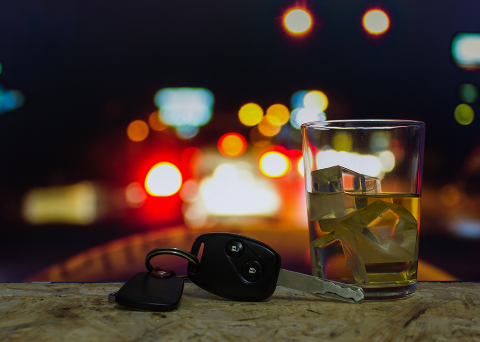Car keys and glass of alcohol on bar with red lights in the background.