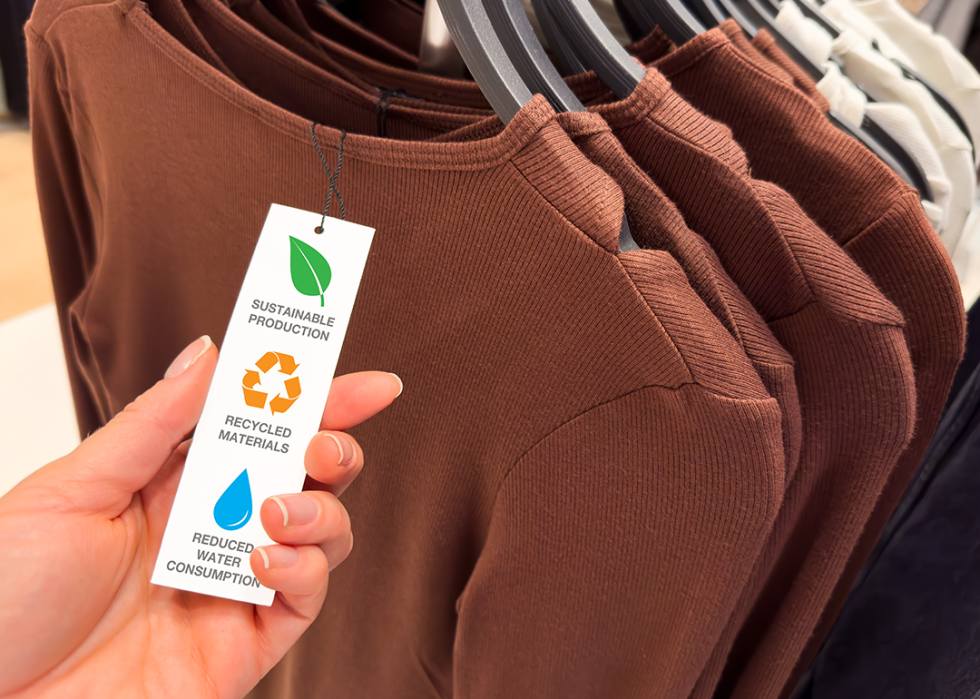 Person looks at a sustainable fashion tag on clothing rack.