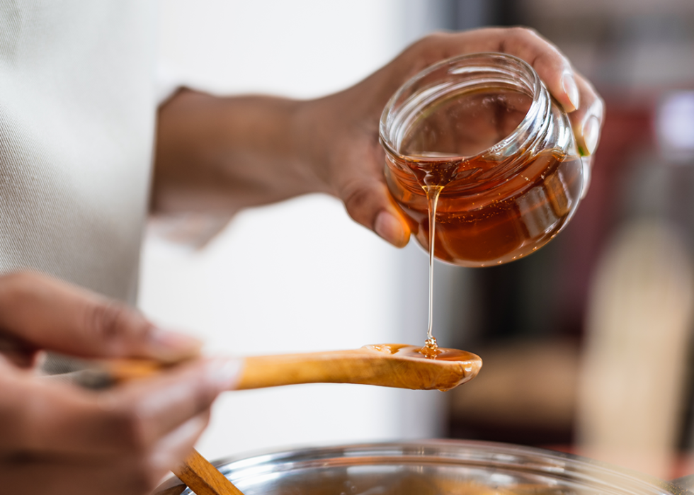 Hands pouring honey from jar to wooden spoon.