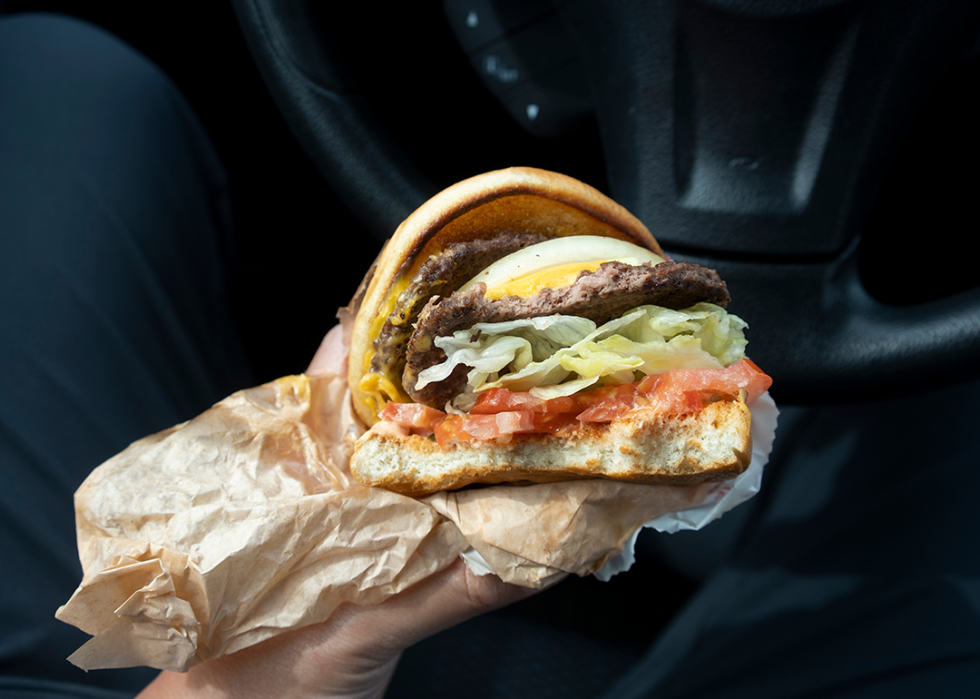 Hand holding fast-food burger in wrapper.