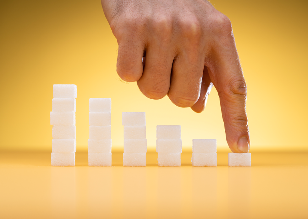 A finger pointing to the smallest sugar cube in a line of sugar cubes.