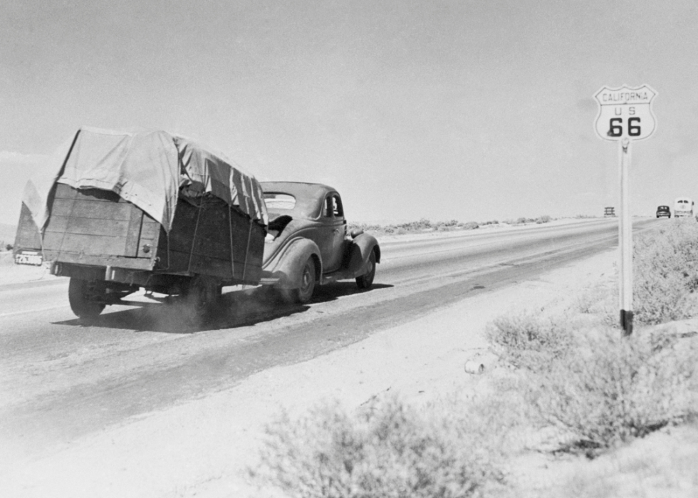 Car pulling trailer past California U.S. 66 road signs.