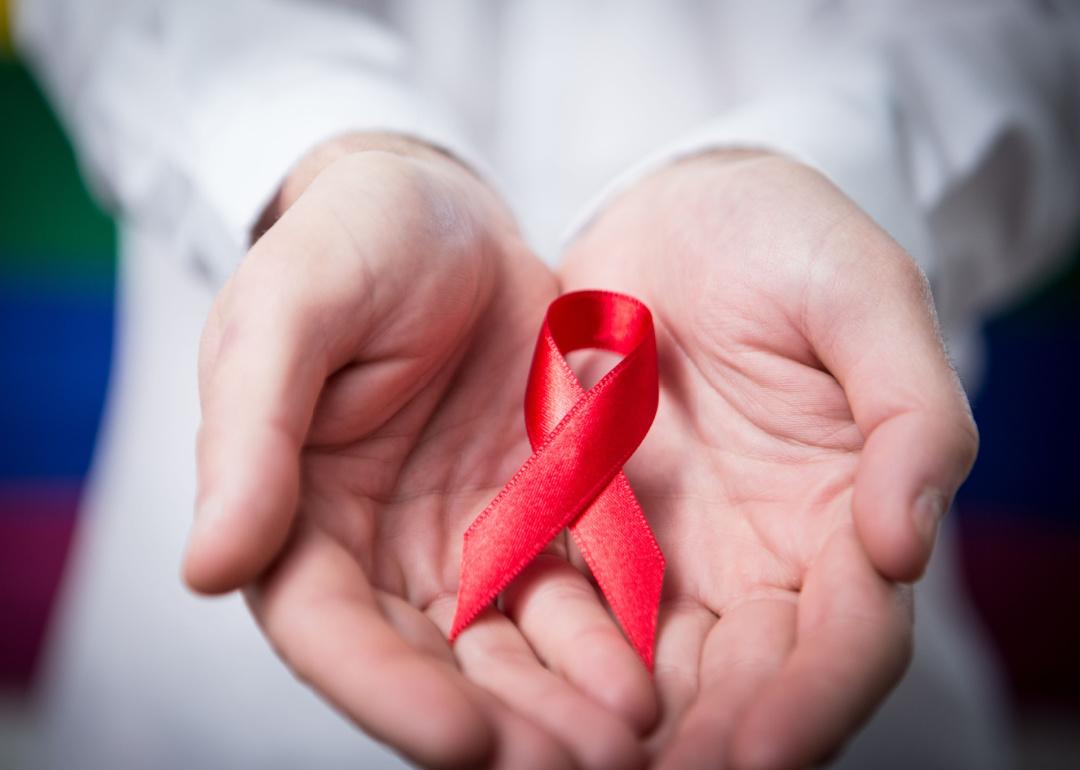 Hands holding red aids awareness ribbon on rainbow background