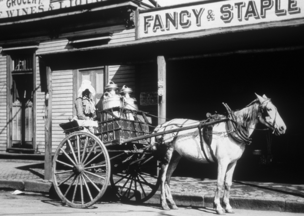 Horse drawn milk wagon in front of stores