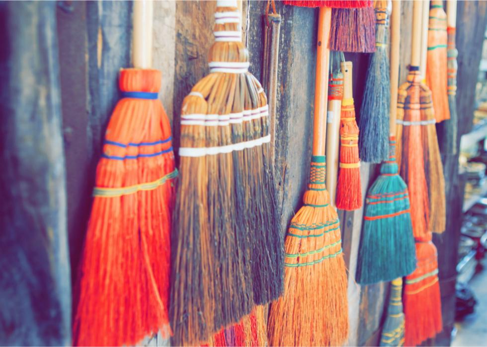 A collection of colorful brooms hanging on a wooden wall.