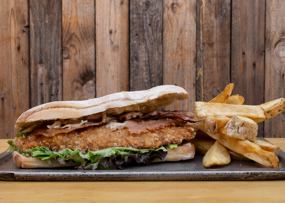 Chicken fried steak sandwich with bacon, cheese, lettuce, and fried potatoes.