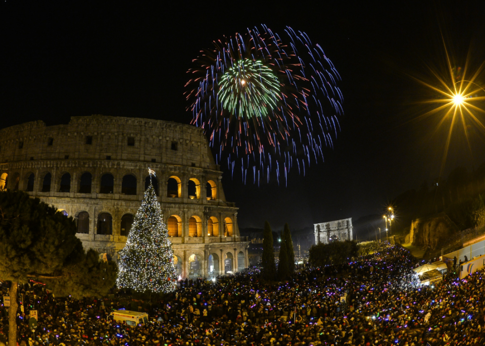 Fireworks over the colosseum and a large Christmas tree in a crowd of people. 
