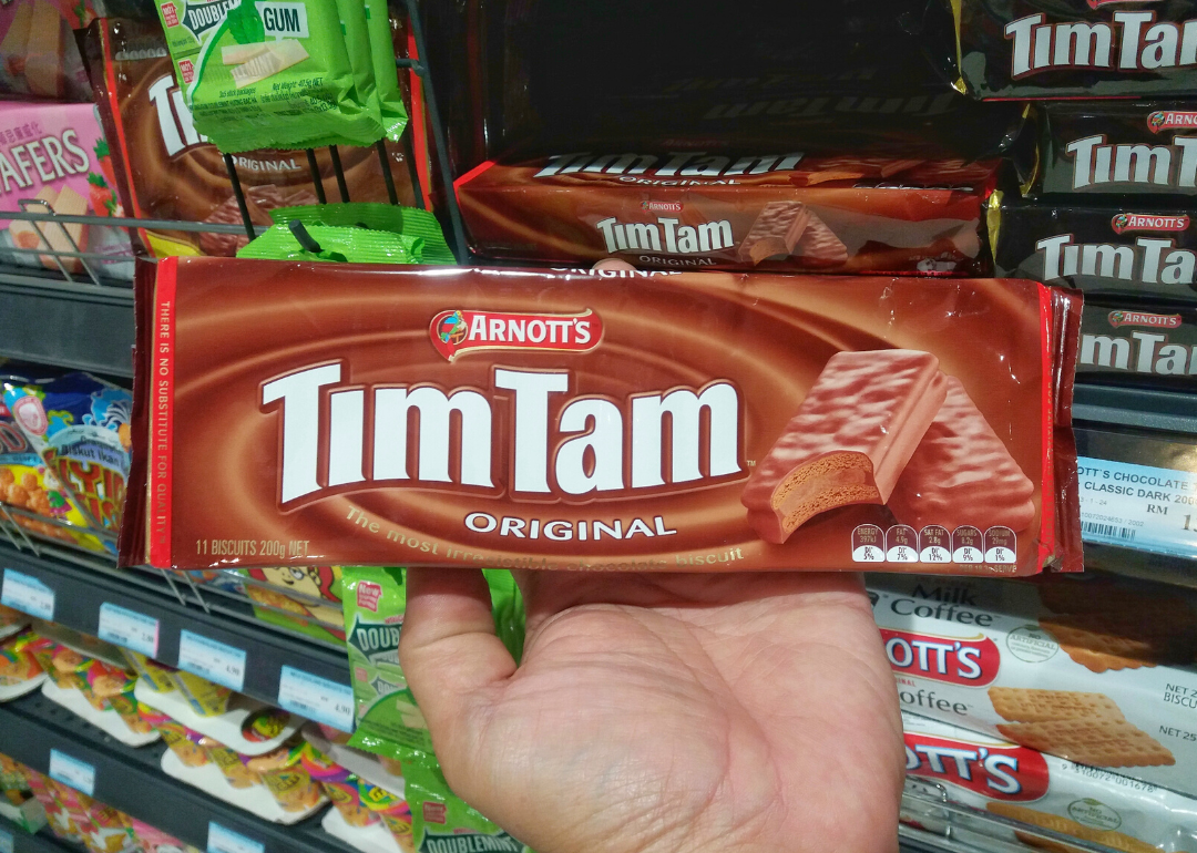 Hand holding a Tim Tam package in a supermarket.