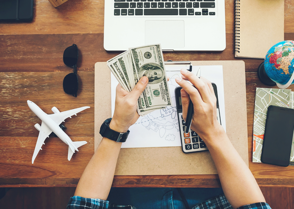 Top view person holding cash and planning trip with calculator.