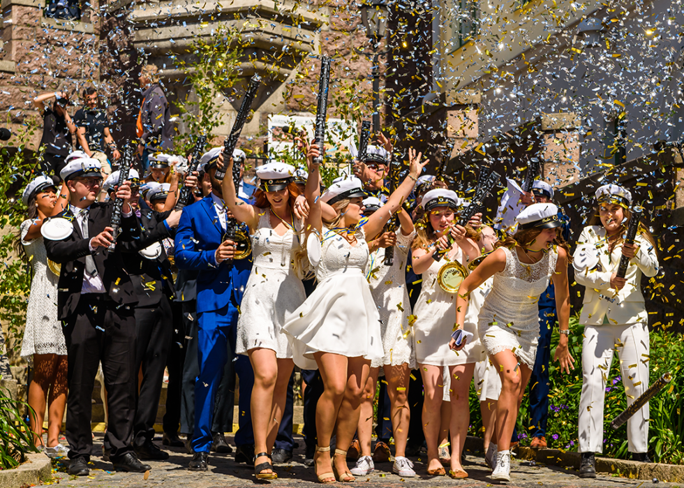 Students wearing hats celebrate graduation with confetti.