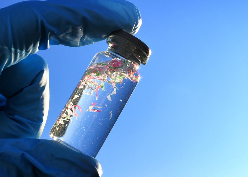Glass vial with water samples contaminated with microplastics against blue sky.