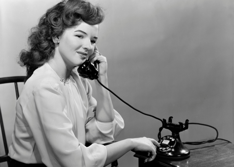 Seated woman talking on rotary telephone.