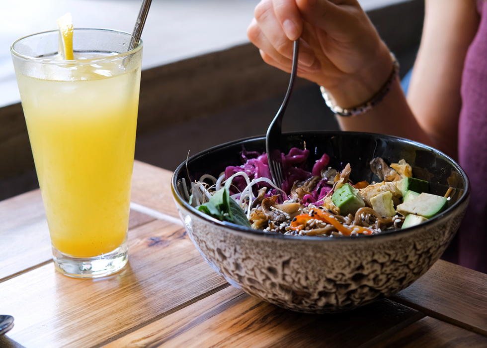 Person eating vegan bowl at cafe with a glass of juice on the table.