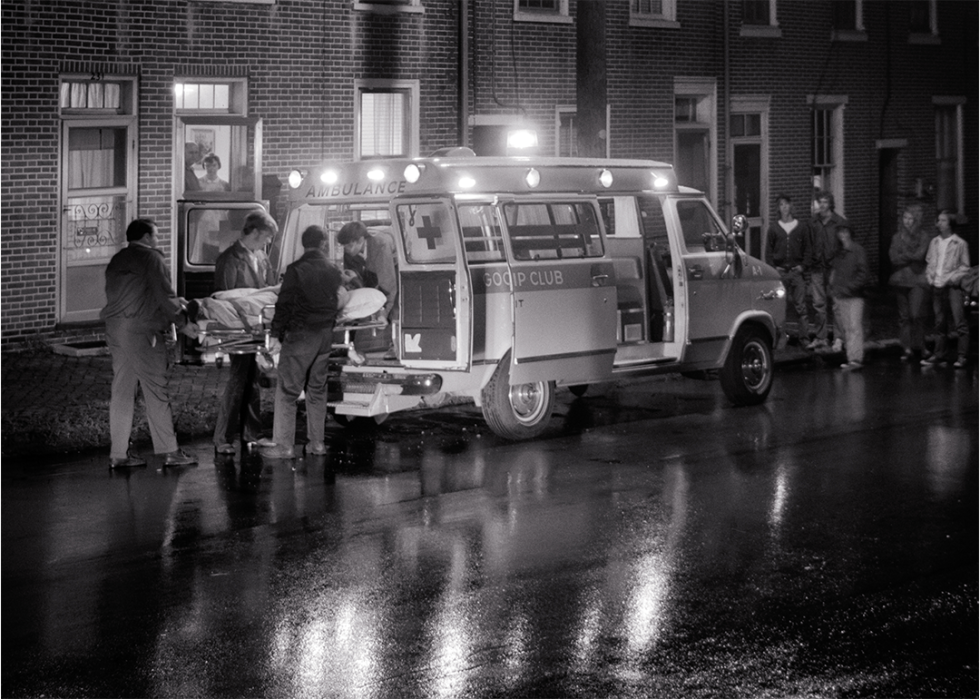 Emergency personnel loading a stretcher with patient into an ambulance at night.