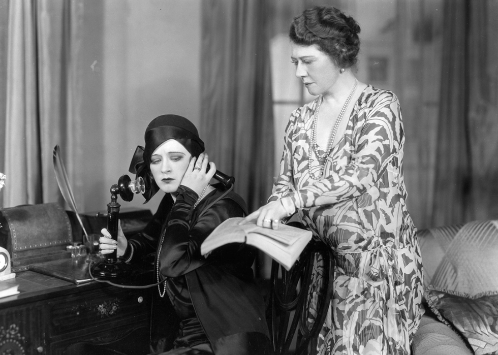 A woman makes a telephone call, while her companion points out the number in a directory.