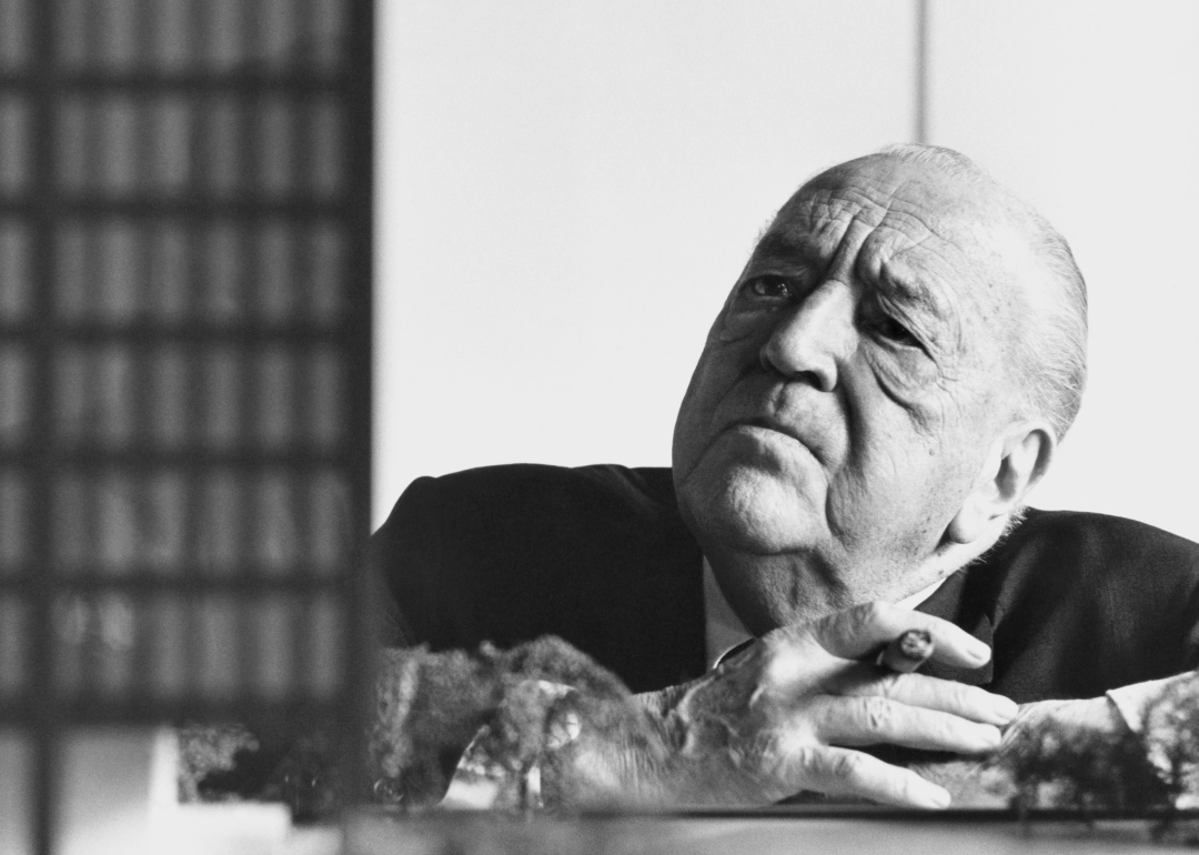 Ludwig Mies van der Rohe looking at architectural model holding cigar.