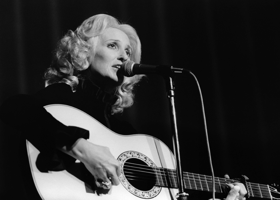 Tammy Wynette singing with guitar at microphone.