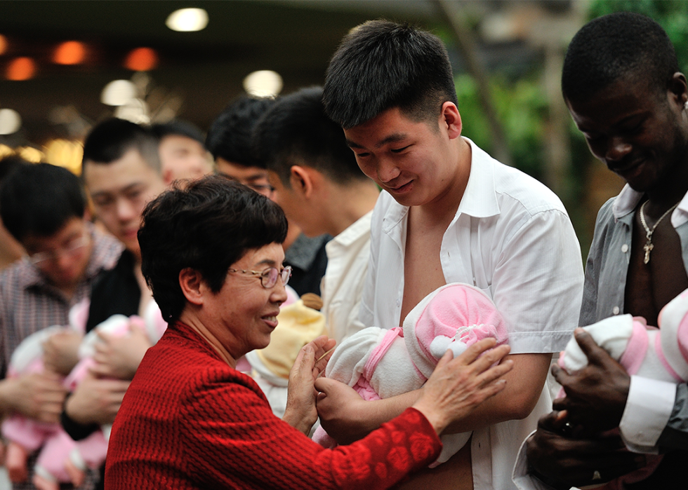 Men holding dolls learn about breastfeeding at a Mother’s Day event.