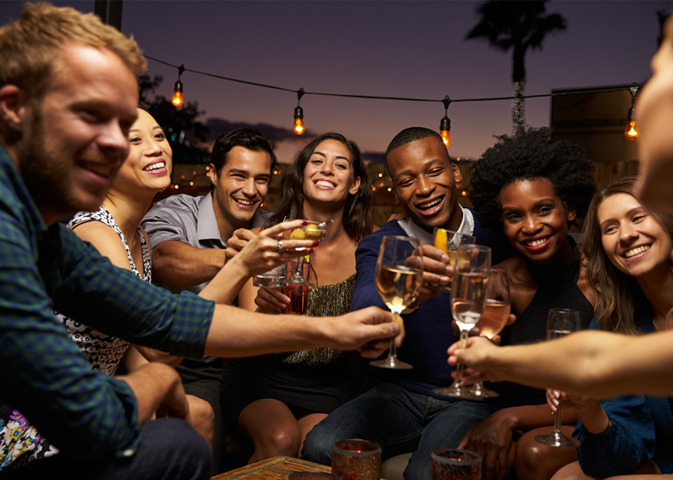 Happy friends toast glasses at evening rooftop party.