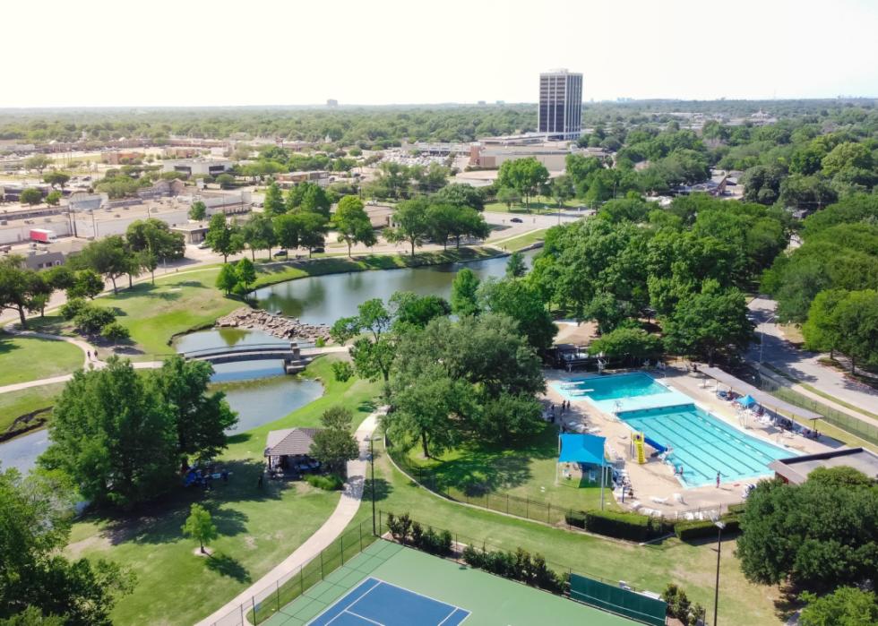 Elevated view of tennis court and swimming pool in recreation park with Richardson, Texas in background.