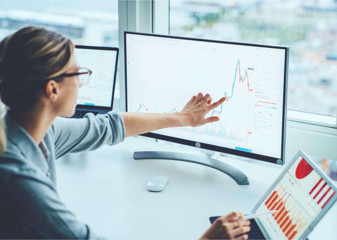 Woman pointing to financial chart on computer screen.