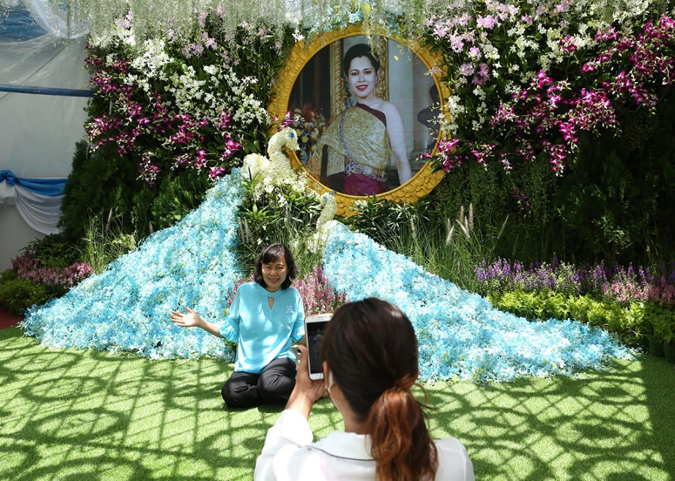 A woman poses for photos in front of the portrait of Queen Sirikit.