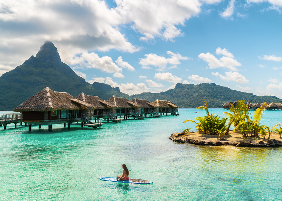 Person paddleboarding near overwater bungalows with Mount Otemanu in background.