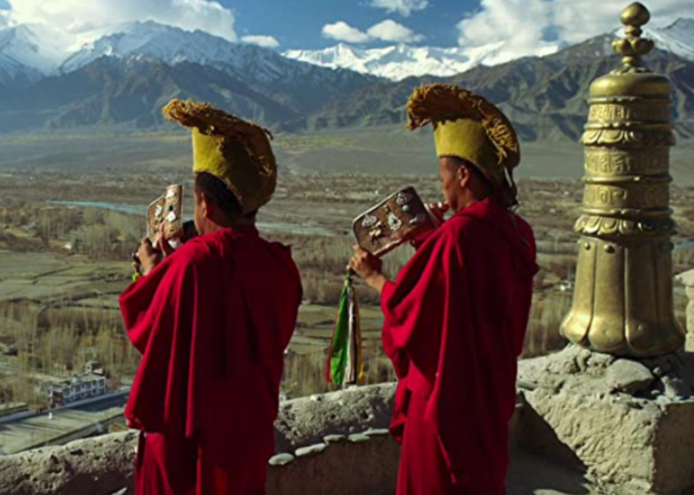Two Tibetan monks with musical instruments looking across a landscape