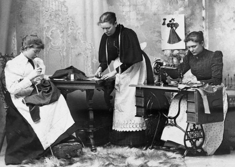 Three young women sew dresses in a shop