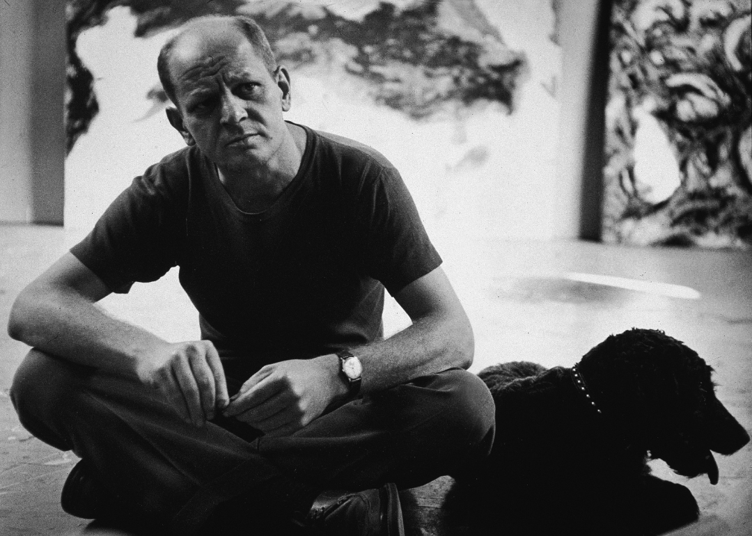 Jackson Pollock sits with a black dog in his studio.