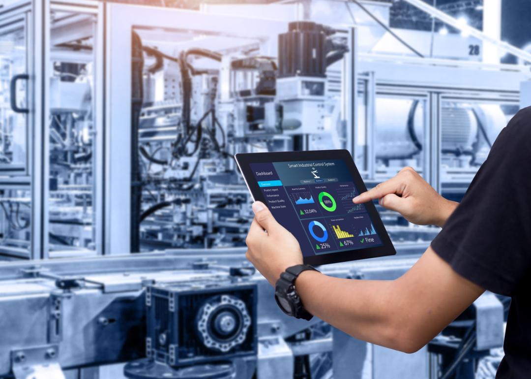 Person holding tablet in automated manufacturing facility.