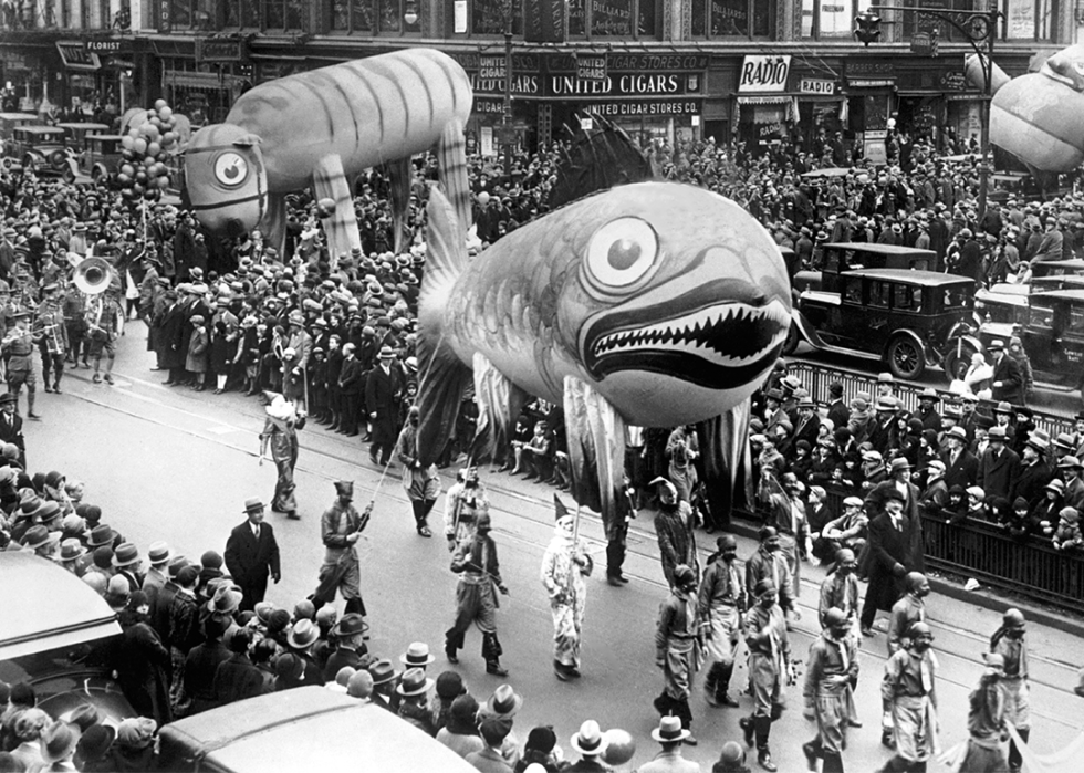 A group of clowns holding two huge balloons, one a tiger and the other a fish with sharp teeth, make their way through crowds along Broadway.