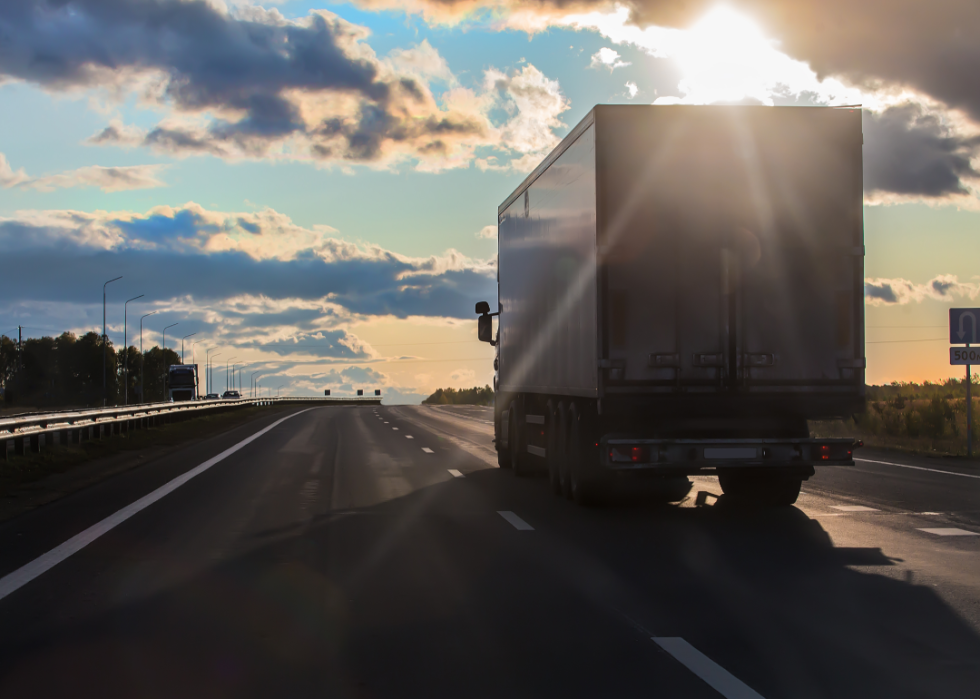 A semi truck drives toward a sunset on an empty highway