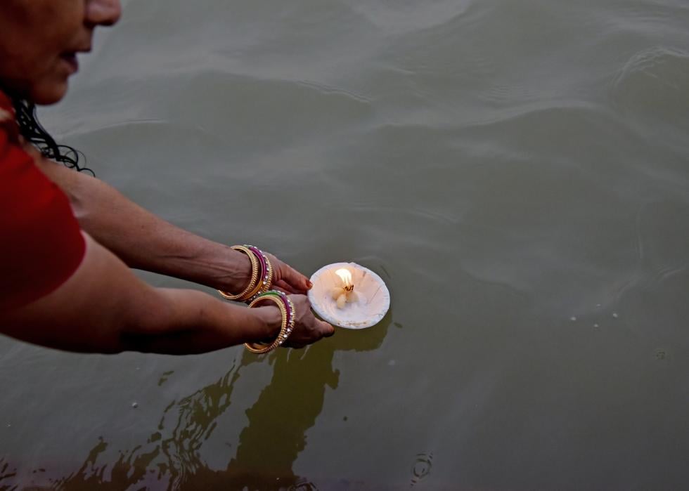 A person placing a lit, floating candle in a river. 