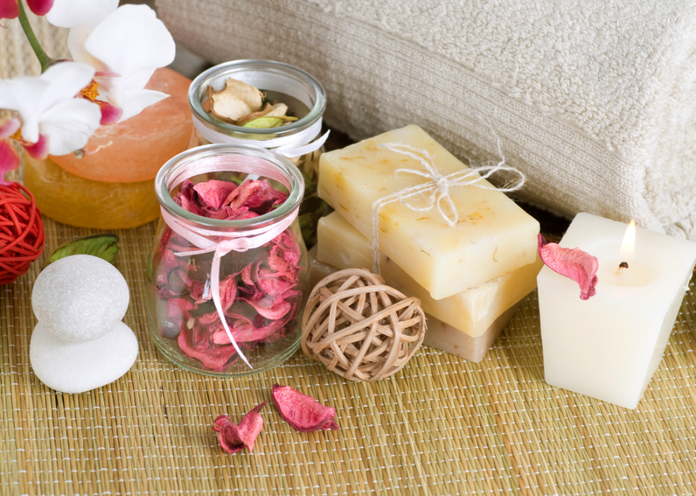 A selection of bath-related items, including soap, dried rose petals, and a towel on a bamboo mat.