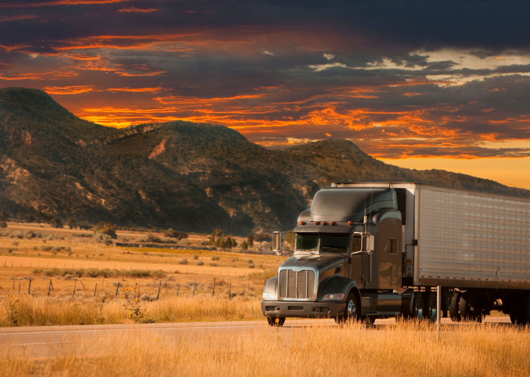 A semi truck passes in front of a mountain range at sunset