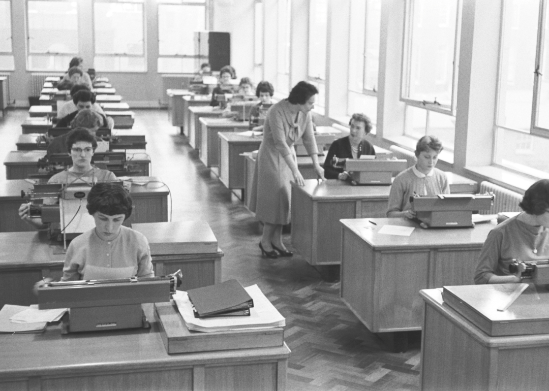 Women converse in a typing pool in a shared office space.