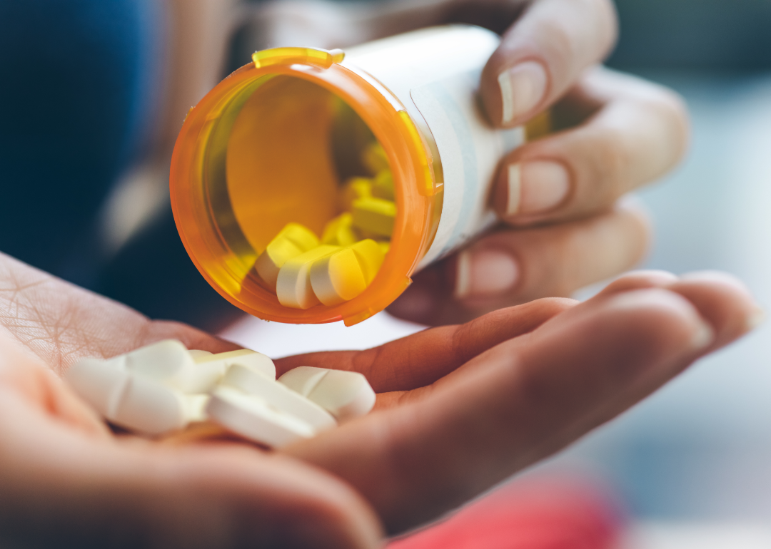 A close up of a person pouring pills from a prescription bottle into their hand.