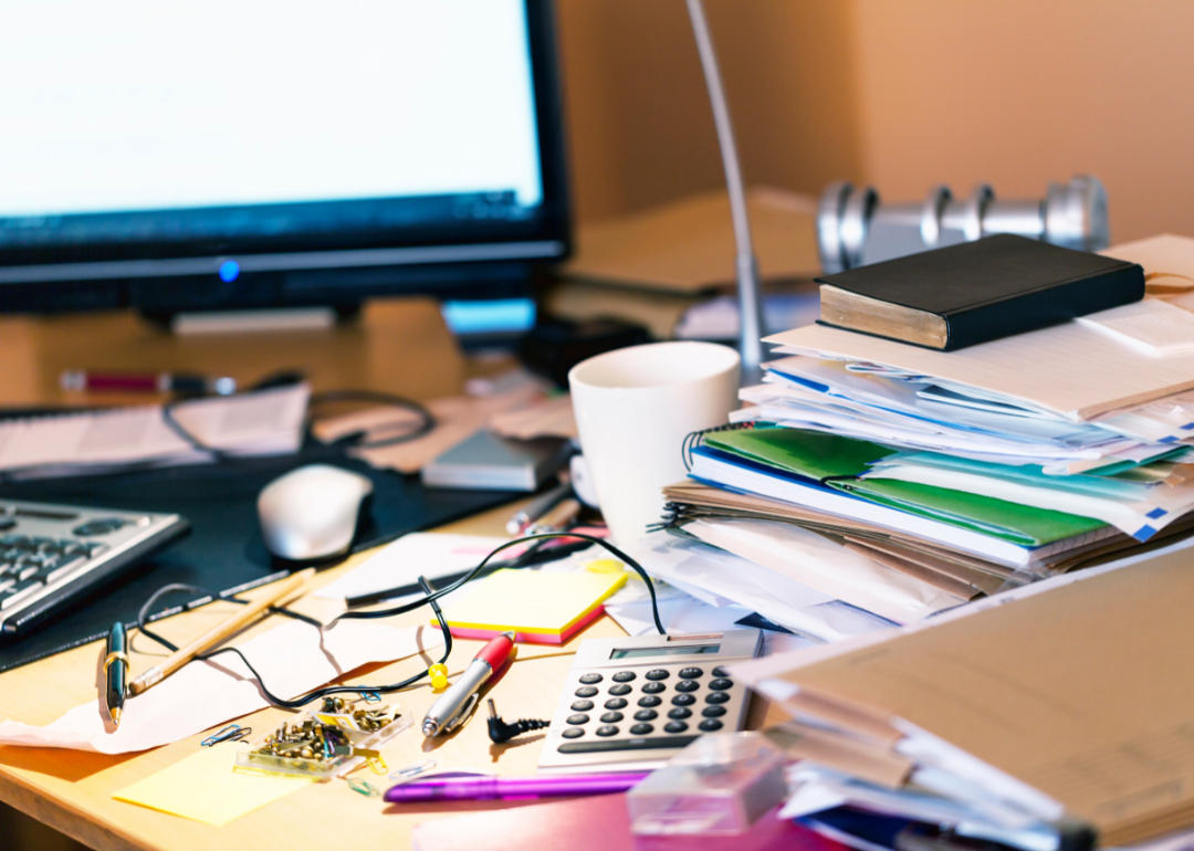 A cluttered desk with stacked documents and assorted junk.