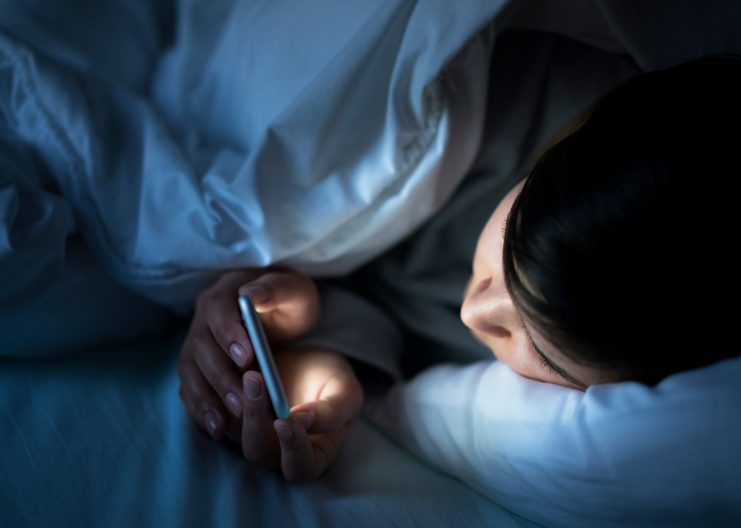 A teen in a dark room is illuminated by her mobile phone