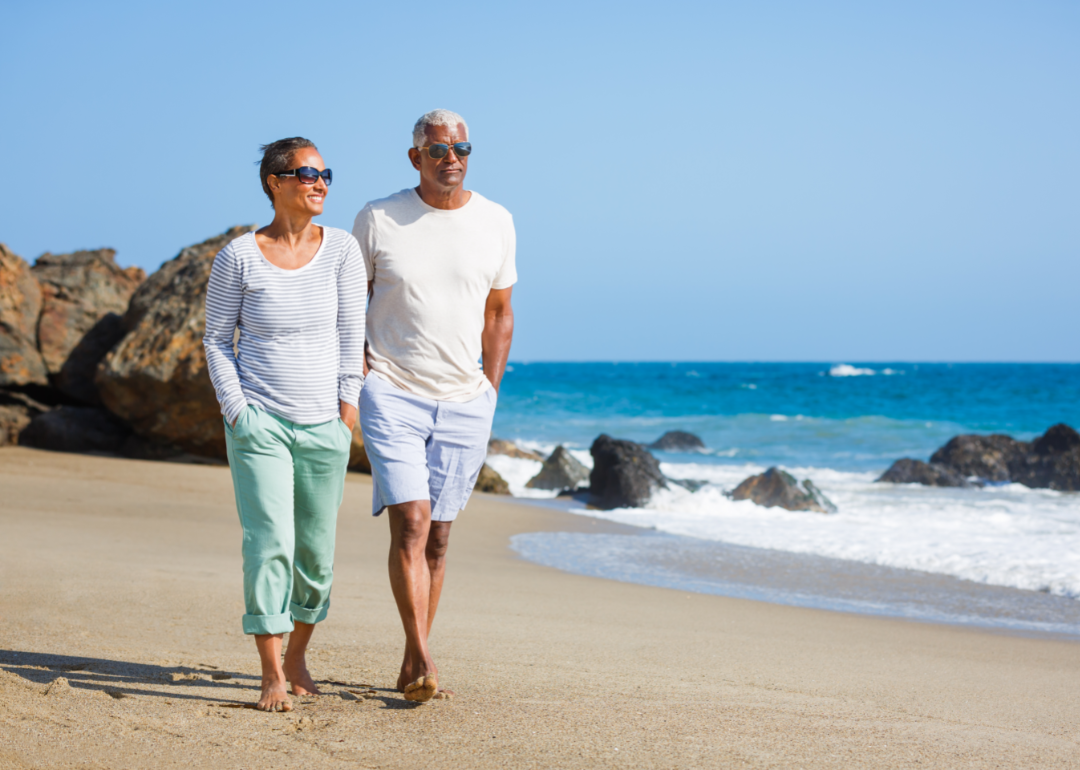 An older couple walking together along a beach.
