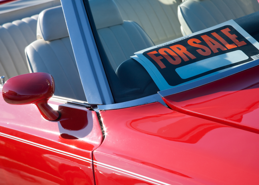 A red convertible with a for sale sign in the window.
