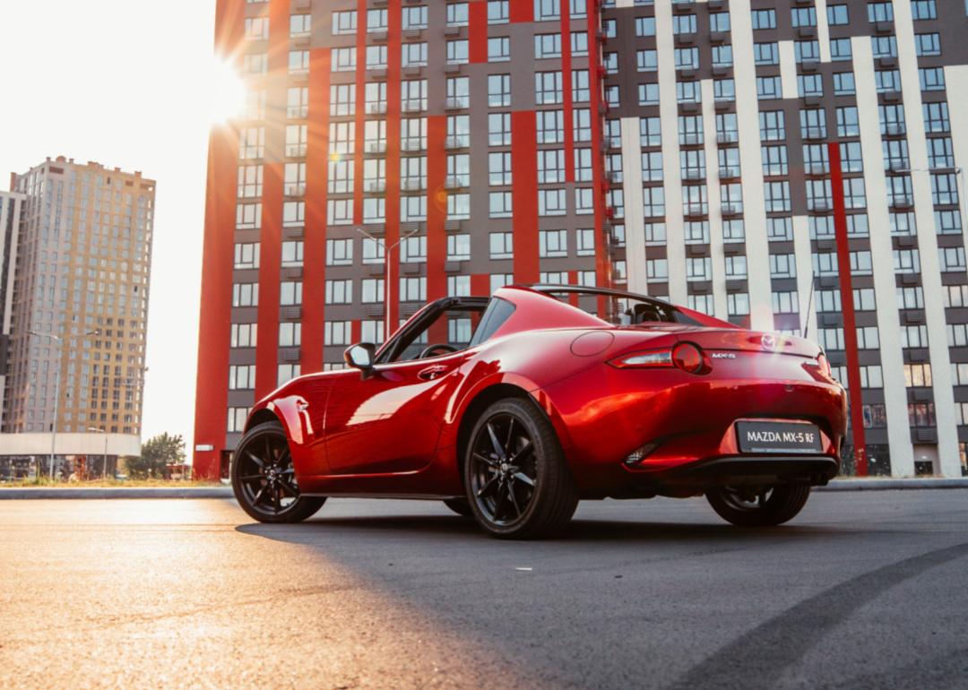 A red Mazda MX-5 is parked in front of a modern building.